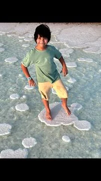 Boy steps on crystallized salt formation, with bright sunlight highlighting Stock Photos