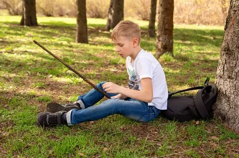 A boy with a stick sits on the grass in a spring park Stock Photos