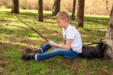 A boy with a stick sits on the grass in a spring park Stock Photos