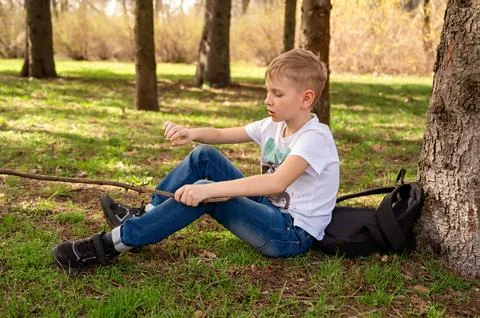 A boy with a stick sits on the grass in a spring park Stock Photos