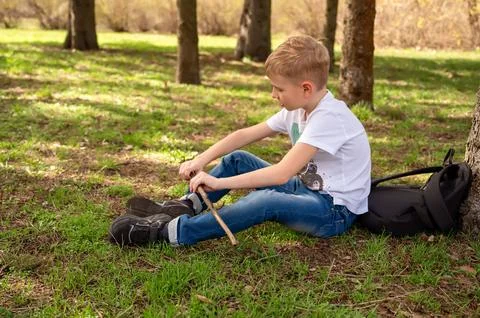 A boy with a stick sits on the grass in a spring park Stock Photos