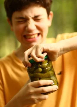 Boy with strain grimace try to remove cover from cucumbers jar Stock Photos