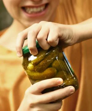 Boy with strain grimace try to remove cover from cucumbers jar Stock Photos