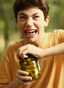 Boy with strain grimace try to remove cover from cucumbers jar Foto stock
