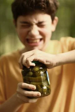 Boy with strain grimace try to remove cover from cucumbers jar Stock Photos