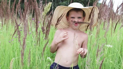 Boy in straw hat walking in vibrant green field surrounded by tall grasses. Video stock 287687661