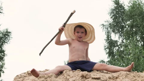 Boy in straw hat waves stick threateningly and throws sand. Stock Footage 287681409