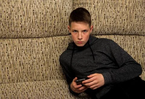 A boy with a strict look lying on the sofa with a phone. Stock Photos