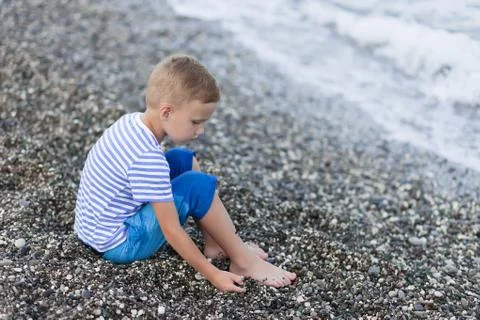 Boy in a striped t-shirt sitting close by the water at the beach Stock Photos