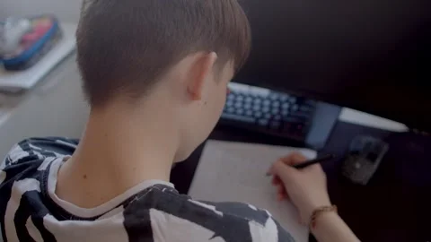 A boy studies at his desk using a computer and taking notes Stock Footage 311205897