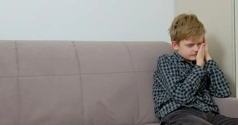 Boy is suffering from toothache sitting on the sofa at home 库存照片