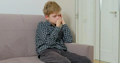 Boy is suffering from toothache sitting on the sofa at home 库存照片