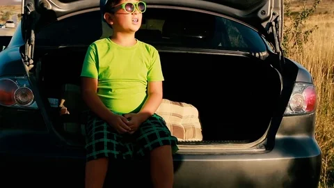 Boy in sunglasses and a cap sits in the trunk of a car Video stock 81115488