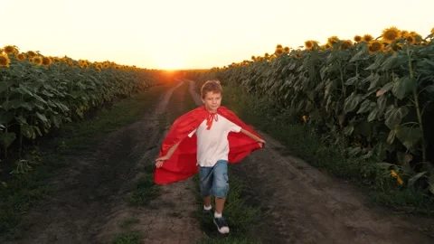 Boy superhero imagination, red cape countryside playtime, child hero sunset Stock Footage 293668096