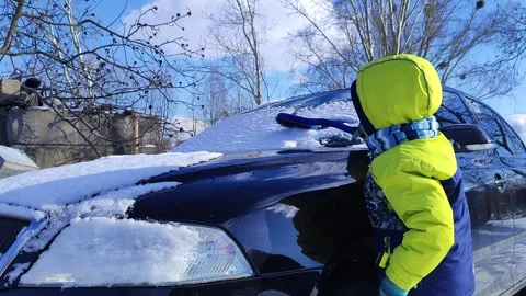 Boy sweeping snow off a car. Boy Cleaning A Car Windshield With Long Broom Video Stock Footage 302513278