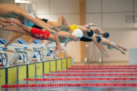 Boy swimmers start from the starting table in the pool Stock Photos