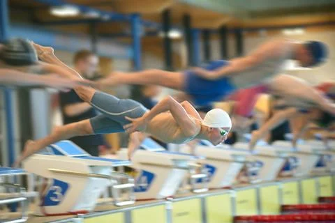 Boy swimmers start from the starting table in the pool Stock Photos