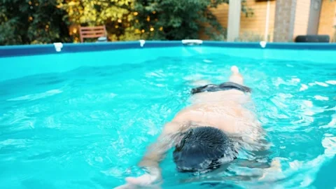 Boy swimming in backyard pool with blue water summer day outdoor activity brick 動画素材 312548524