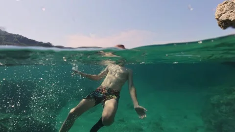 Boy swimming split shot over under half underwater Видео 338180942