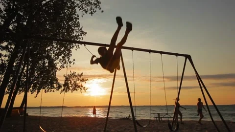 A boy swinging on the beach at sunset Stock Footage 158999624