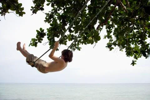 Boy swinging by ocean Stock Photos