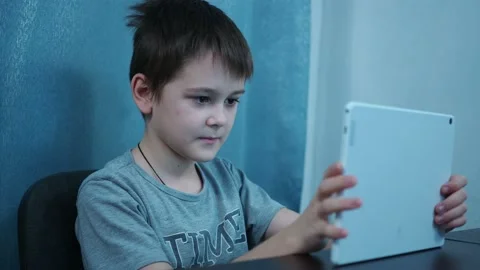 A boy in a t-shirt flips through social networks on a white tablet sitting at a Stock Footage 144263031