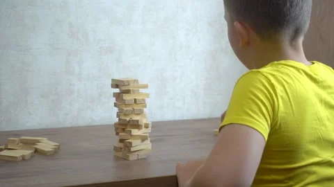 The boy at the table builds a tower of wooden dominoes Video stock 160988448