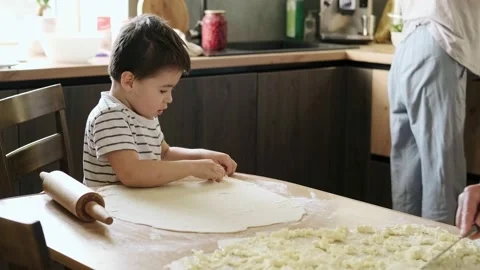 Boy at the table in the kitchen helping grandmother cooking from dough. Family Stock Footage
