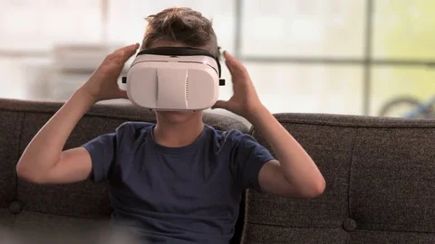 Boy takes off virtual reality headset on the couch Stock Footage 79573330