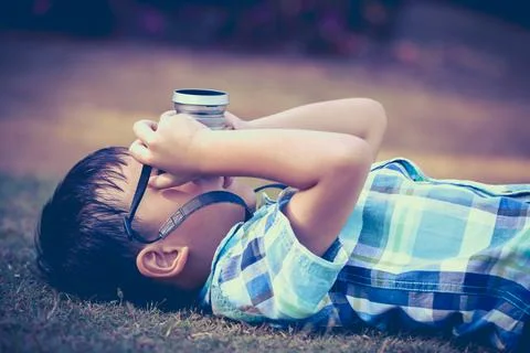 Boy taking photo by camera, exploring nature at park. Concepts of creativity. Stock Photos