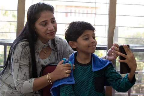 Boy taking selfie while getting haircut from mother at home Photos