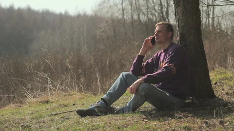 Boy talking on a cell phone,tourist,guy tired,boy sitting under a tree Video stock 48689954