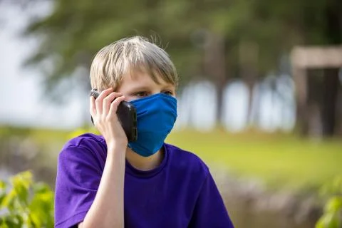 Boy talking on phone while wearing a homemade face mask to help him stay heal Stock Photos