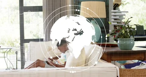 Boy tapping tablet on sofa in technology demo animating globe with orbiting data Stock Footage 318917825
