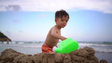 Boy Taps Sand With Watering Can Beside Sandcastle Stock-Footage 344123969