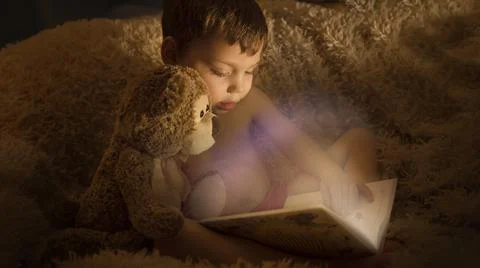 A boy with a teddy bear reading a fairy tale in the dark Stock Photos