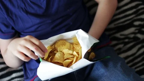 Boy teenager eating potato chips with hands on sofa at home.fast food unhealthy Stock Footage
