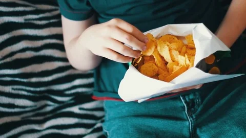 Boy teenager eating potato chips with hands on sofa at home Stock Footage