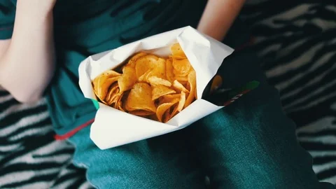 Boy teenager eating potato chips with hands on sofa at home Stock Footage