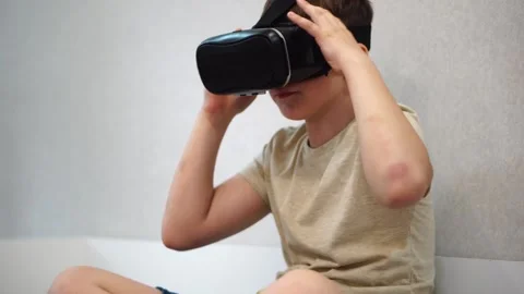 Boy ten years old putting virtual reality helmet on his head sitting on bed in h Stock Footage 307488882