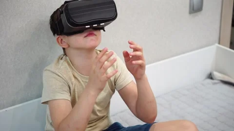 Boy ten years old using virtual reality helmet sitting on bed in his room. close Stock Footage 307489908