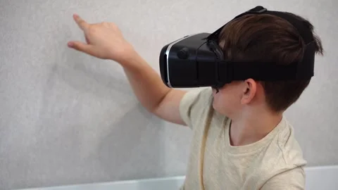 Boy ten years old using virtual reality helmet sitting on bed in his room. close Stock Footage 307490081