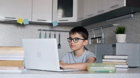Boy with textbooks doing homework at school using a laptop at home. Online Stock Footage 127924725