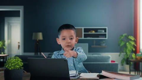 Boy with textbooks doing school homework online talks with teacher using tablet Video stock 139771202