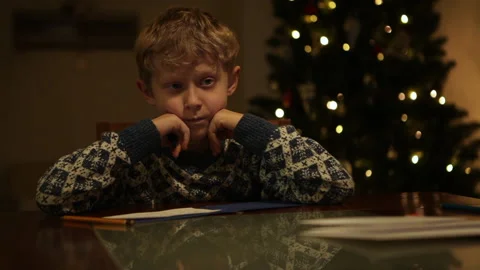 Boy thinking a lot about his wishes to Santa and writing down their in letter Stock-Footage 144491590
