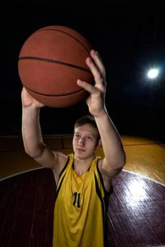 A boy throws a basketball while playing basketball in a dark gym. Stock Photos