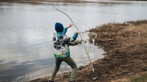 A boy throws a long branch into the water from the river Bank Stock Footage 128016391