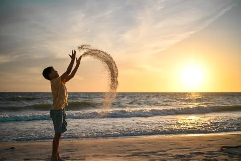 Boy throws sand with curved effect and sunset over ocean Stock Photos
