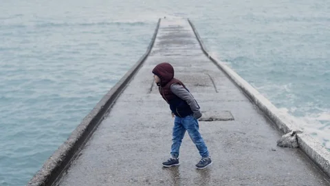 A boy throws a stone from a concrete structure into the blue sea water Stock Footage 128242644