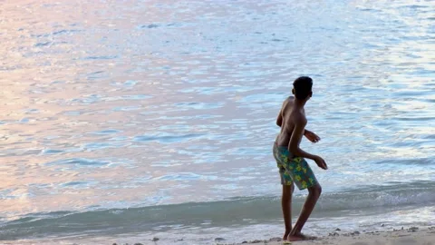 Boy throws stones into the ocean Video stock 169980839